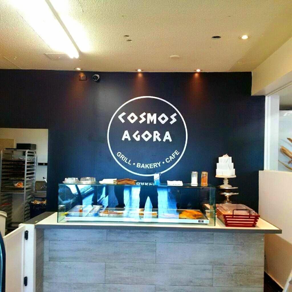 Large wall graphic of Cosmos Agora logo behind the serving counter inside the store
